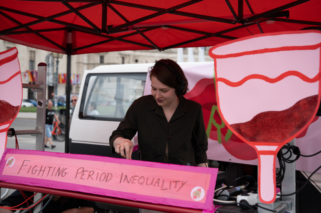 WAVE Rave DJ mixing music in front of a poster that says "fighting period inequality"